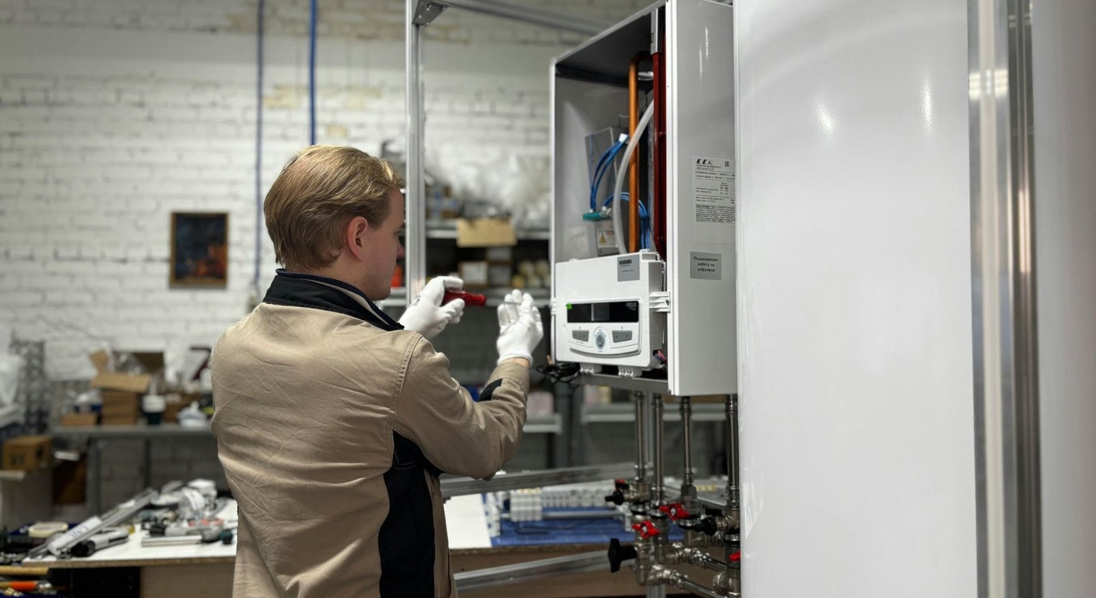 An indoor technician wearing white gloves is pictured working on the open control panel of an indoor heat pump.