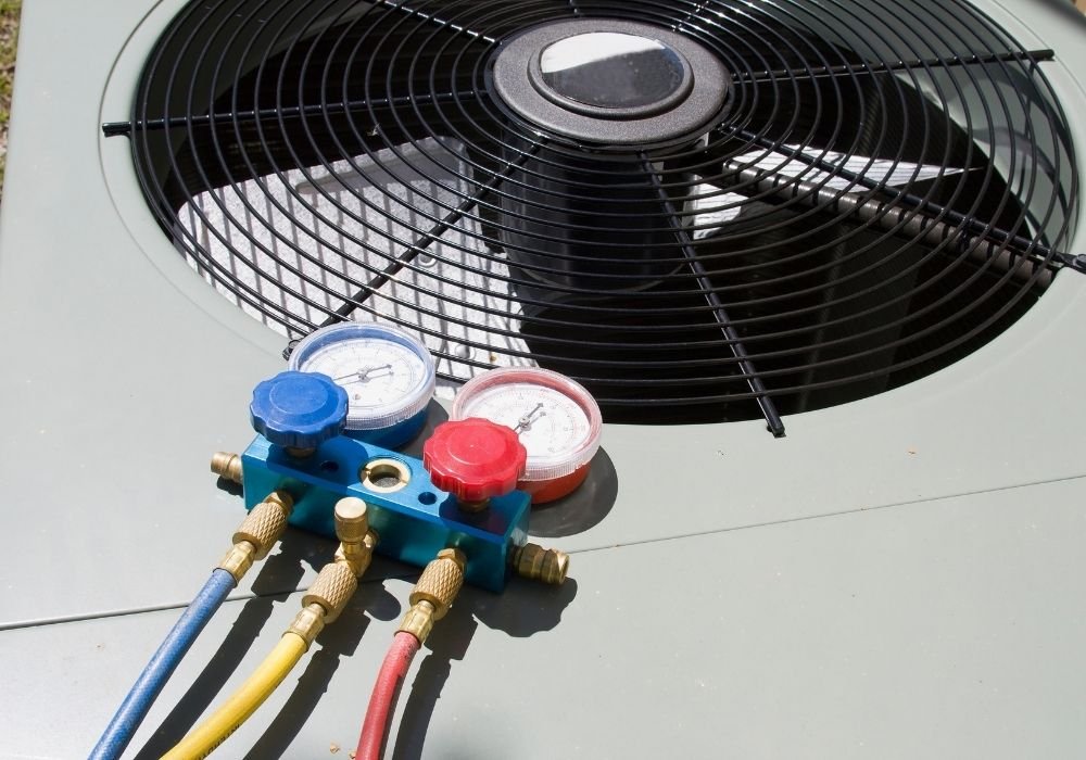 Close-up of professional blue and red manifold gauges connected to the fan grille of a modern outdoor HVAC unit.