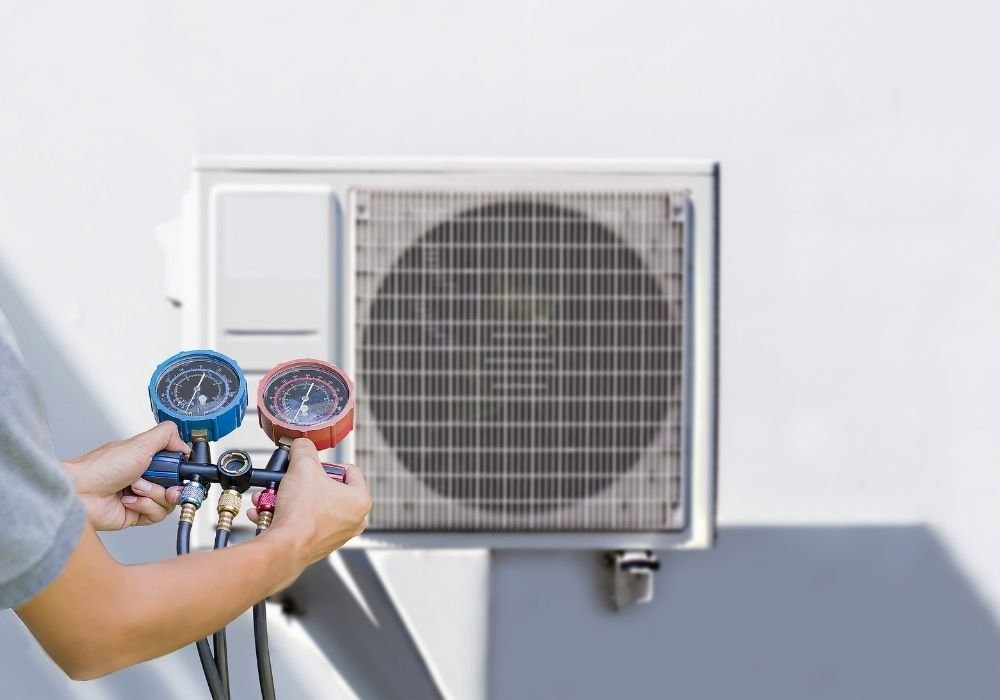 A technician holding professional manifold gauges in front of a modern outdoor heat pump unit to check system pressure.